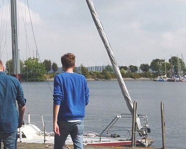 Vier GMSH-Studenten gehen am Kieler Yachthafen entlang. Im Hintergrund ist Wasser und ein Segelboot zu sehen. 