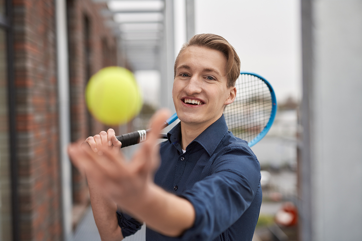 Porträt von Fabian Walter. Er hält einen Tennisschläger und wirft einen Tennisball hoch. 