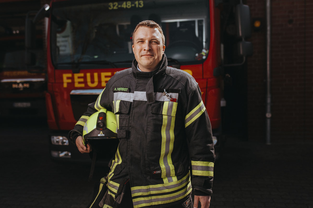 Andreas Herbst steht in Feuerwehruniform vor einem Feuerwehrwagen. 