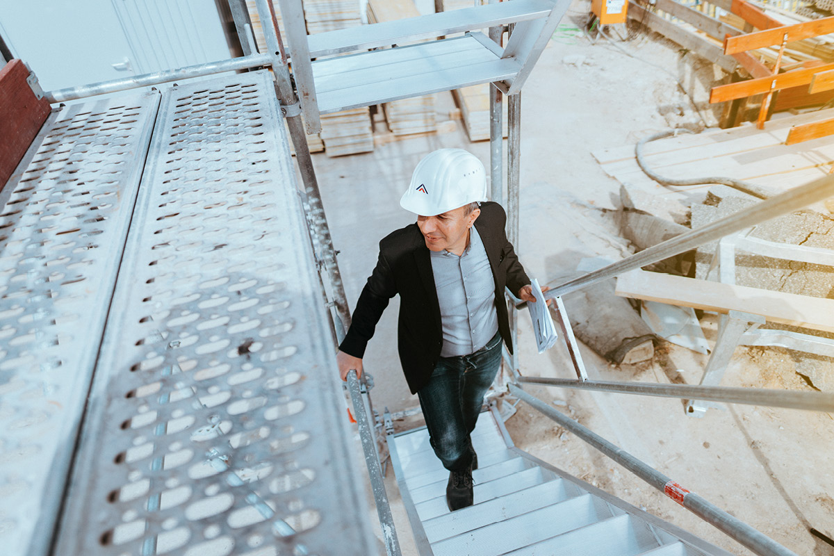 GMSH-Projektmanager Metin Toksöz auf der Baustelle Geowissenschaftliches Institut. Er geht eine Treppe aus Lochstahlplatten hinauf.