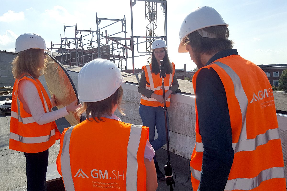 Vier GMSH-Studentinnen unterhalten sich auf einem Gebäudedach. Sie tragen Warnwesten und Bauhelme. 