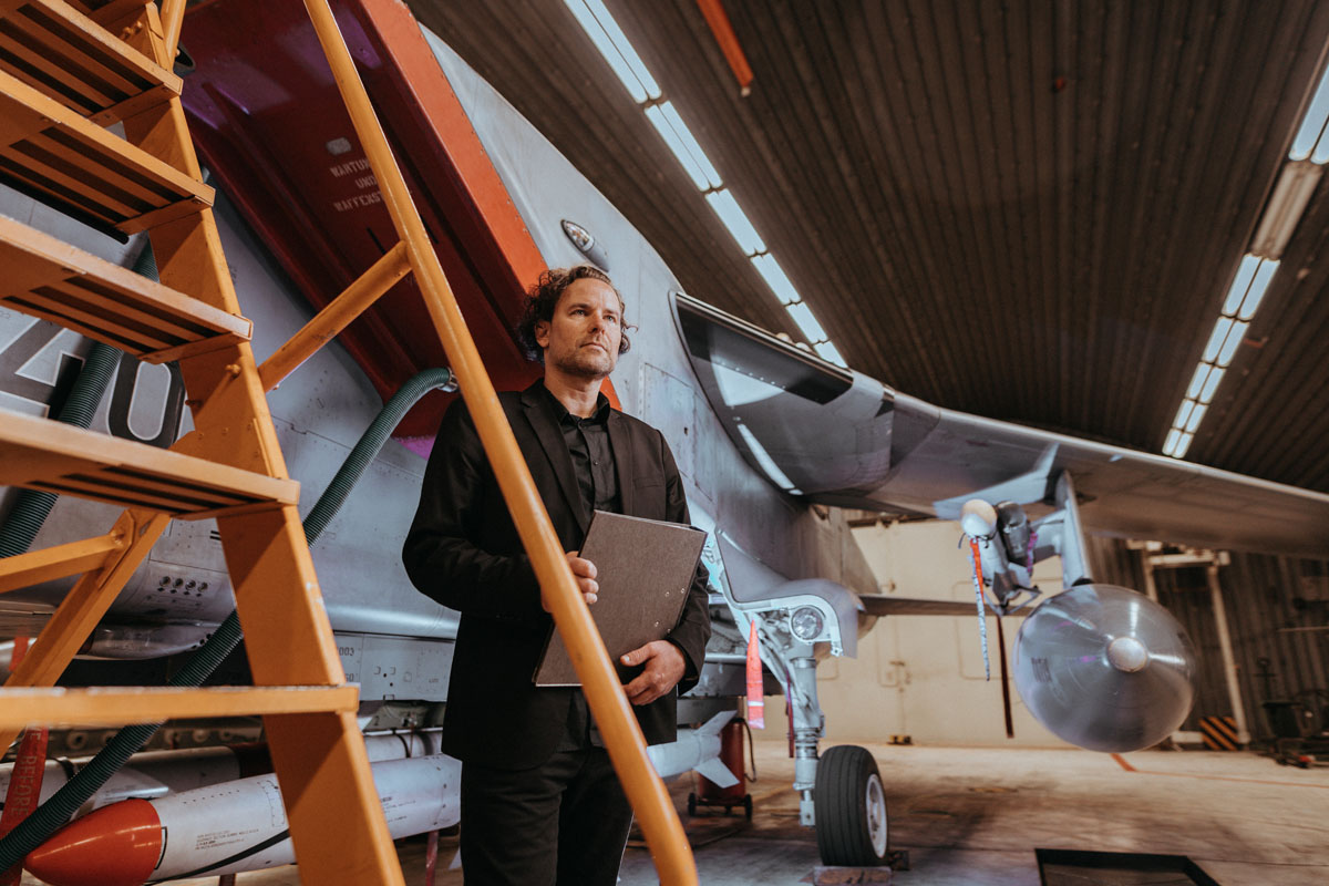 GMSH-Projektleiter Thomas Friedrich steht in einer Flugzeughalle, im Hintergrund ist ein Kampfjet zu sehen.