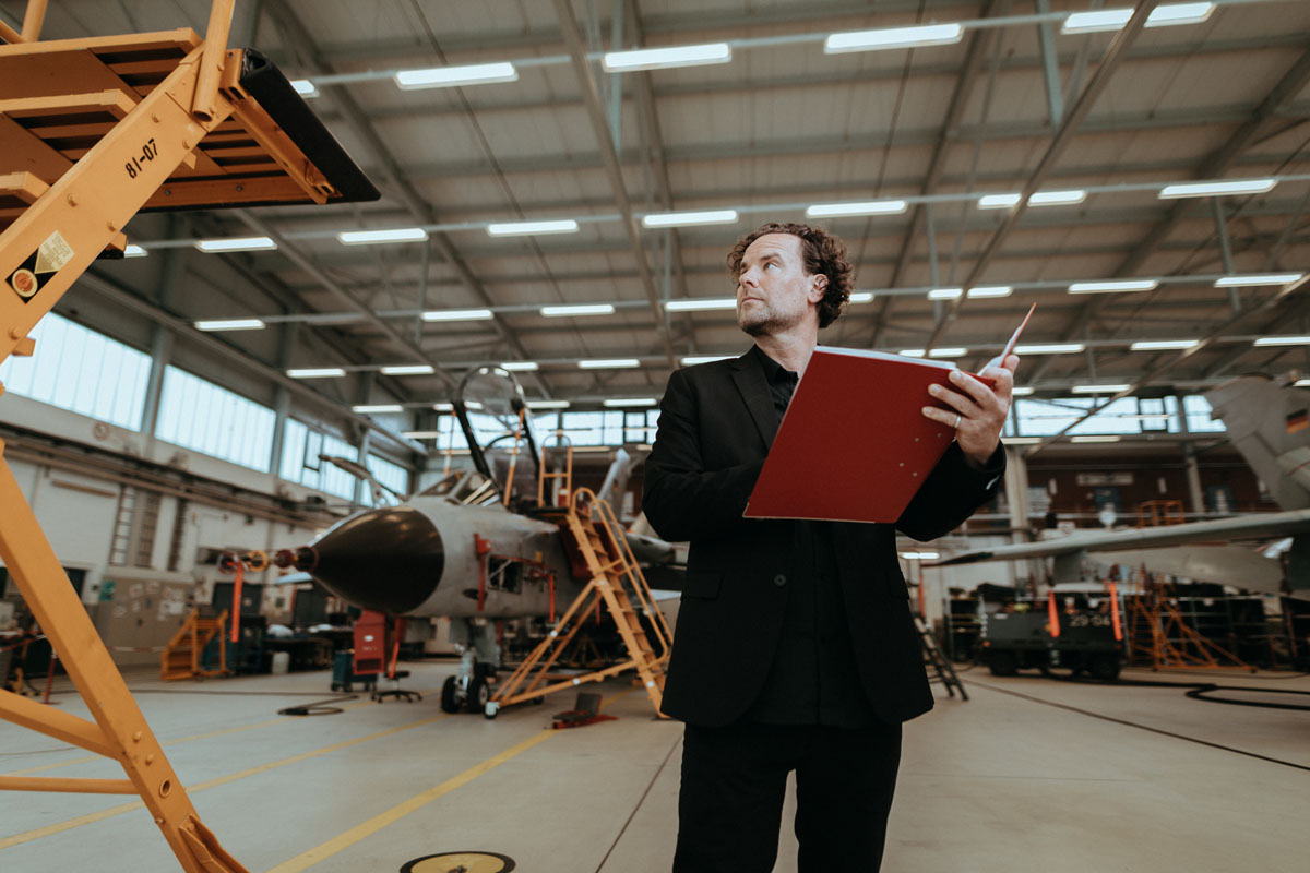GMSH-Projektleiter Thomas Friedrich steht in einer Flugzeughalle, im Hintergrund ist ein Kampfjet zu sehen.